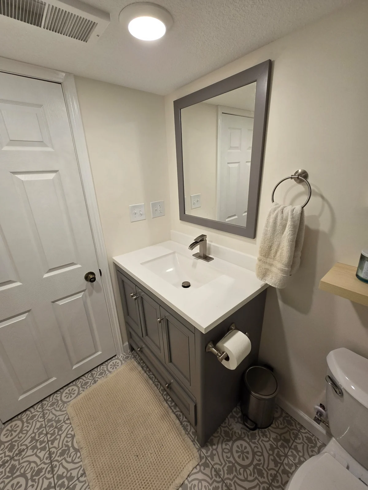 The finished downstairs bathroom vanity, framed mirror, and patterned tile floor.