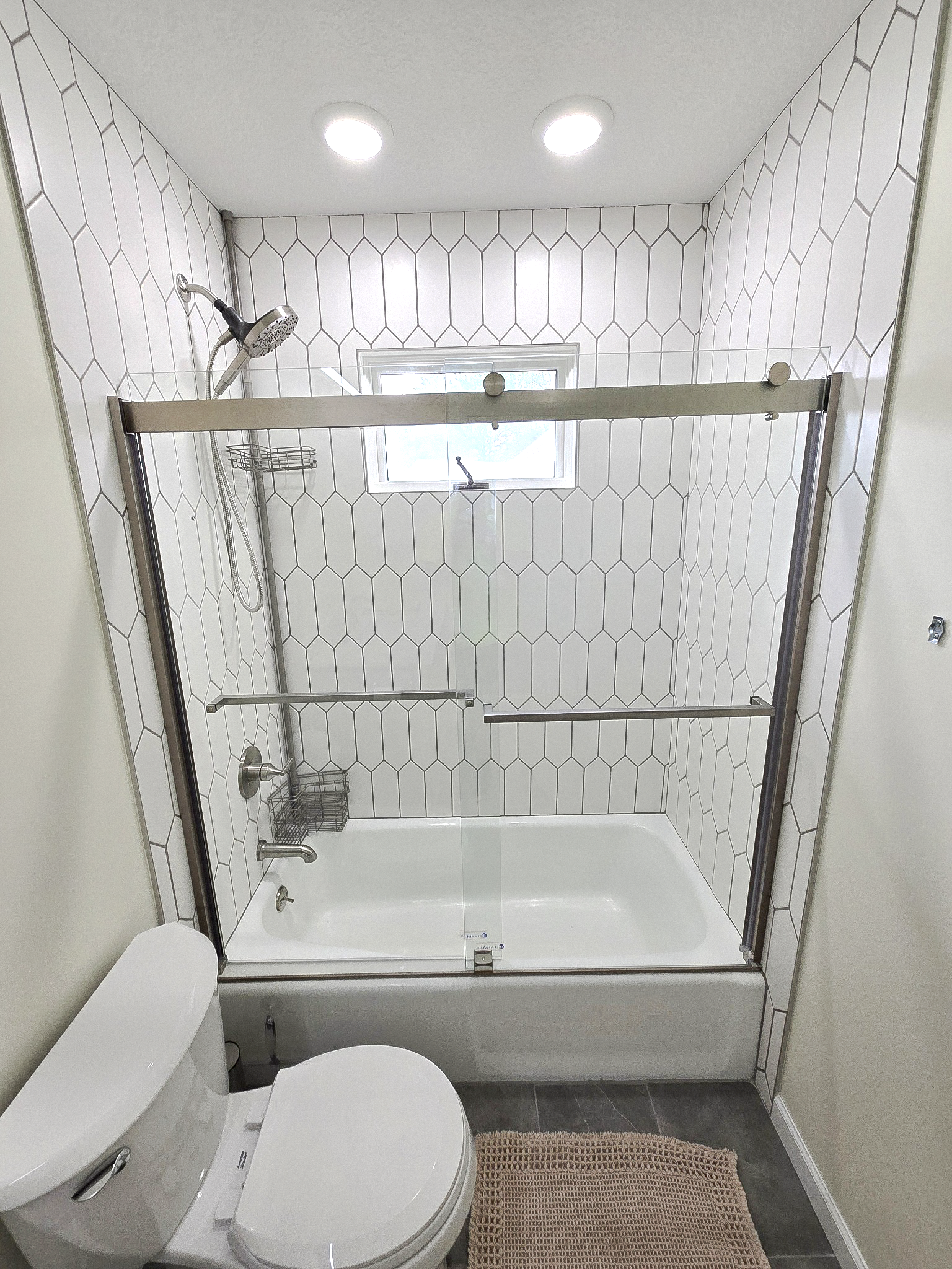 The upstairs bathroom’s retained tub and window, framed by new geometric tile and a glass enclosure.